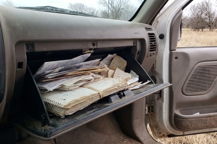 An open truck glovebox stuffed with folded papers, receipts and a notebook